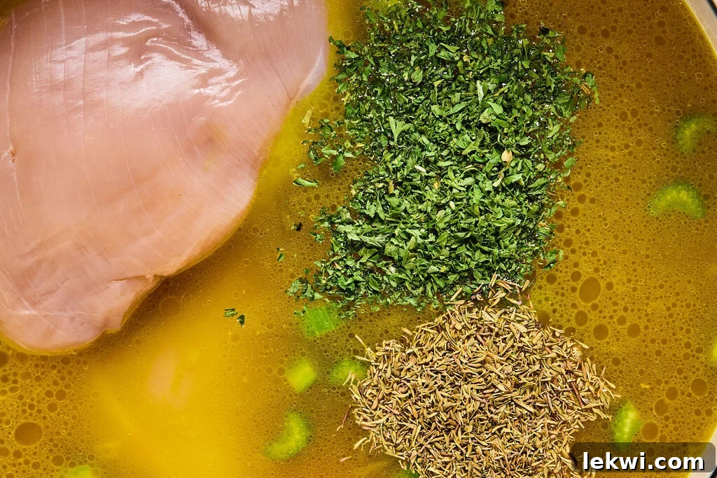 Boneless chicken breast, thyme, and parsley submerged in the simmering soup broth.