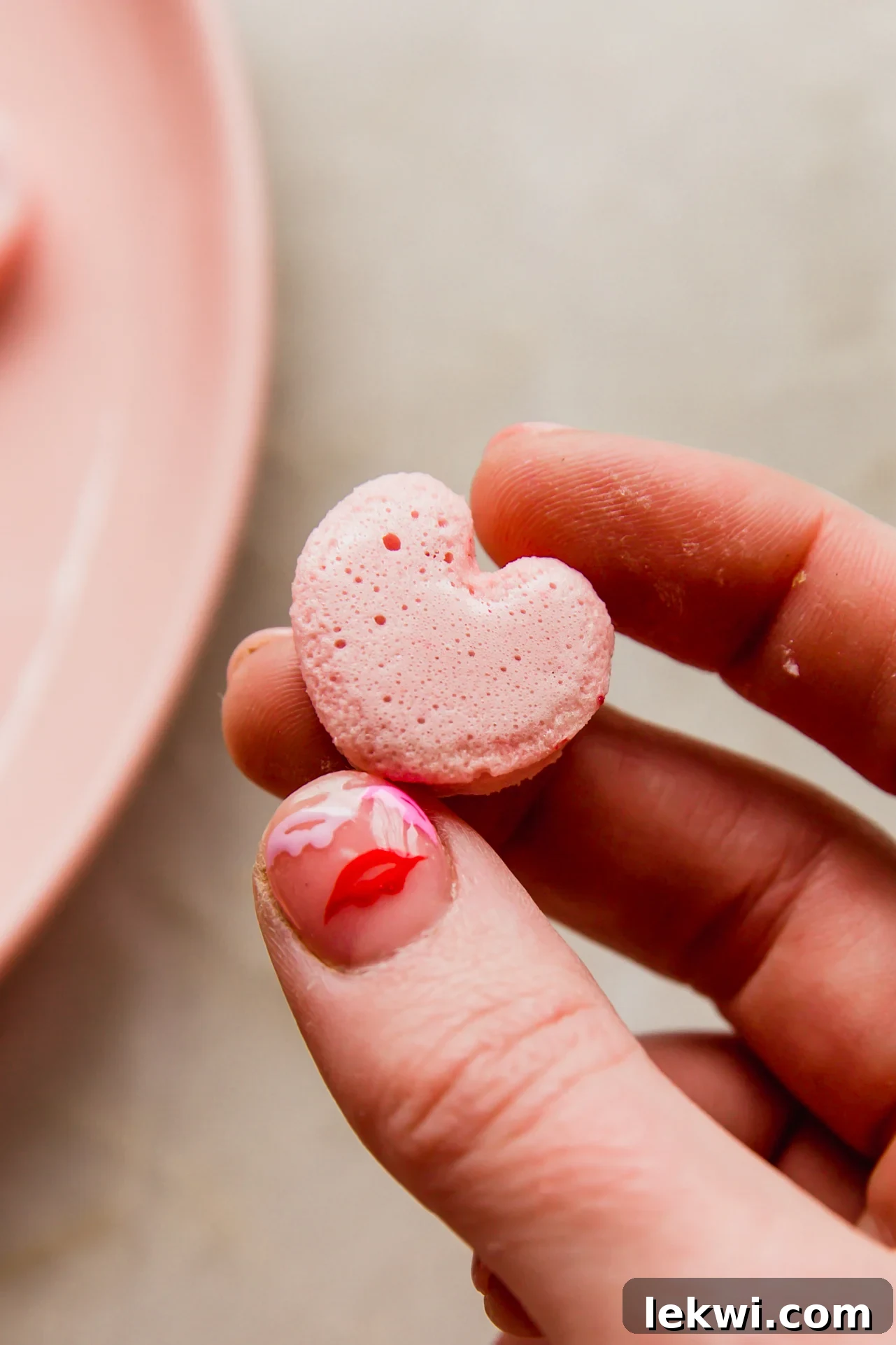 A hand gracefully holding one perfectly shaped homemade heart-shaped pink marshmallow, highlighting its soft, inviting texture and natural vibrant color against a blurred background.