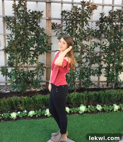 A brunette woman in black pants and a pink shirt standing in front of lush greenery at Magnolia Market.