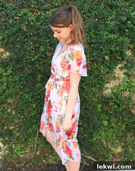 A brunette woman in a floral wrap dress standing in front of a green foliage wall in Austin.