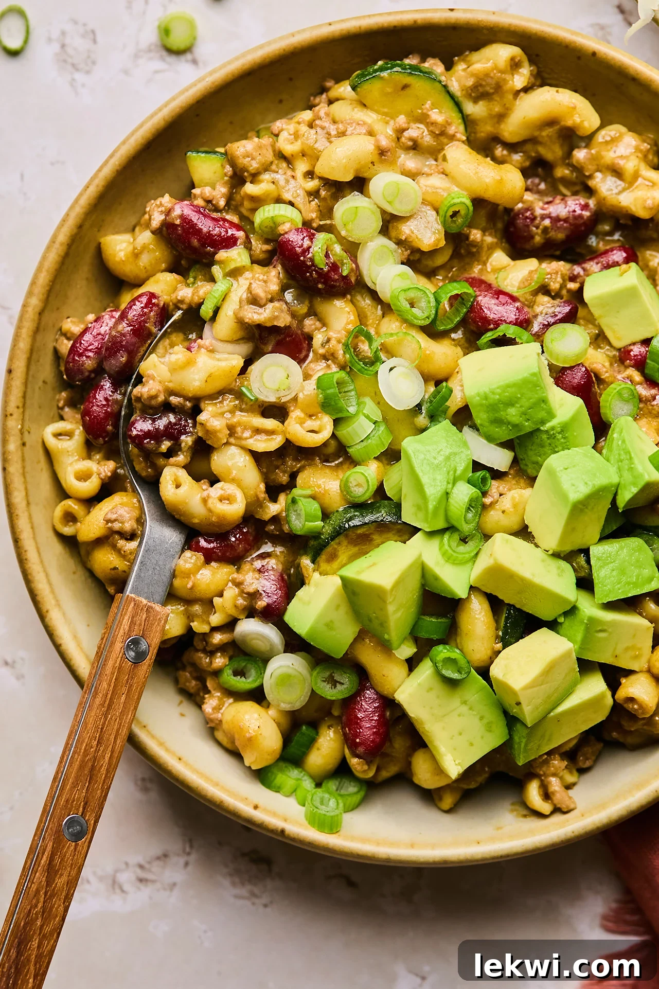 Gluten free chili mac topped with avocado and green onion in a brown bowl.