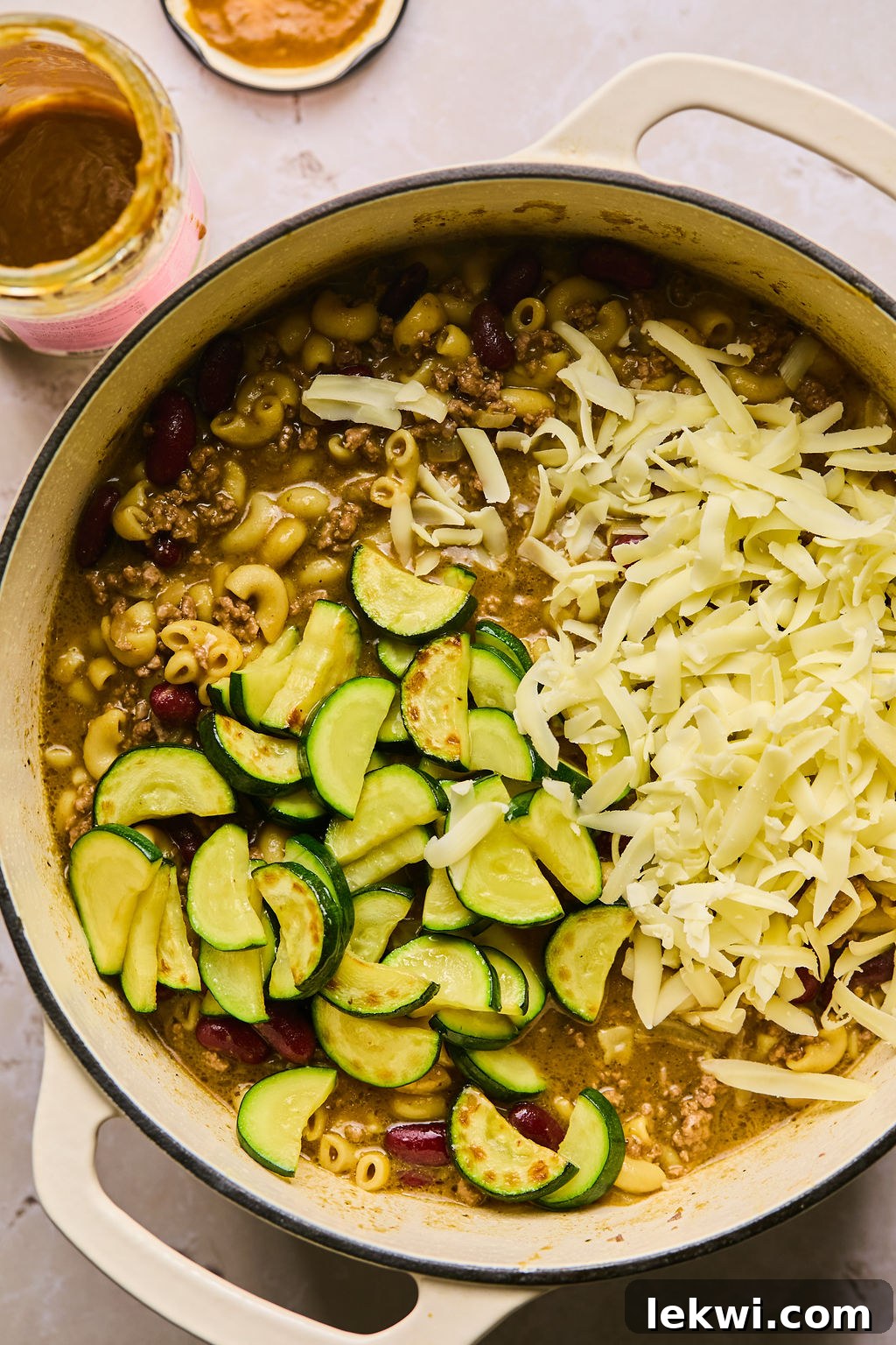 adding zucchini and cheese into the pot with chili mac