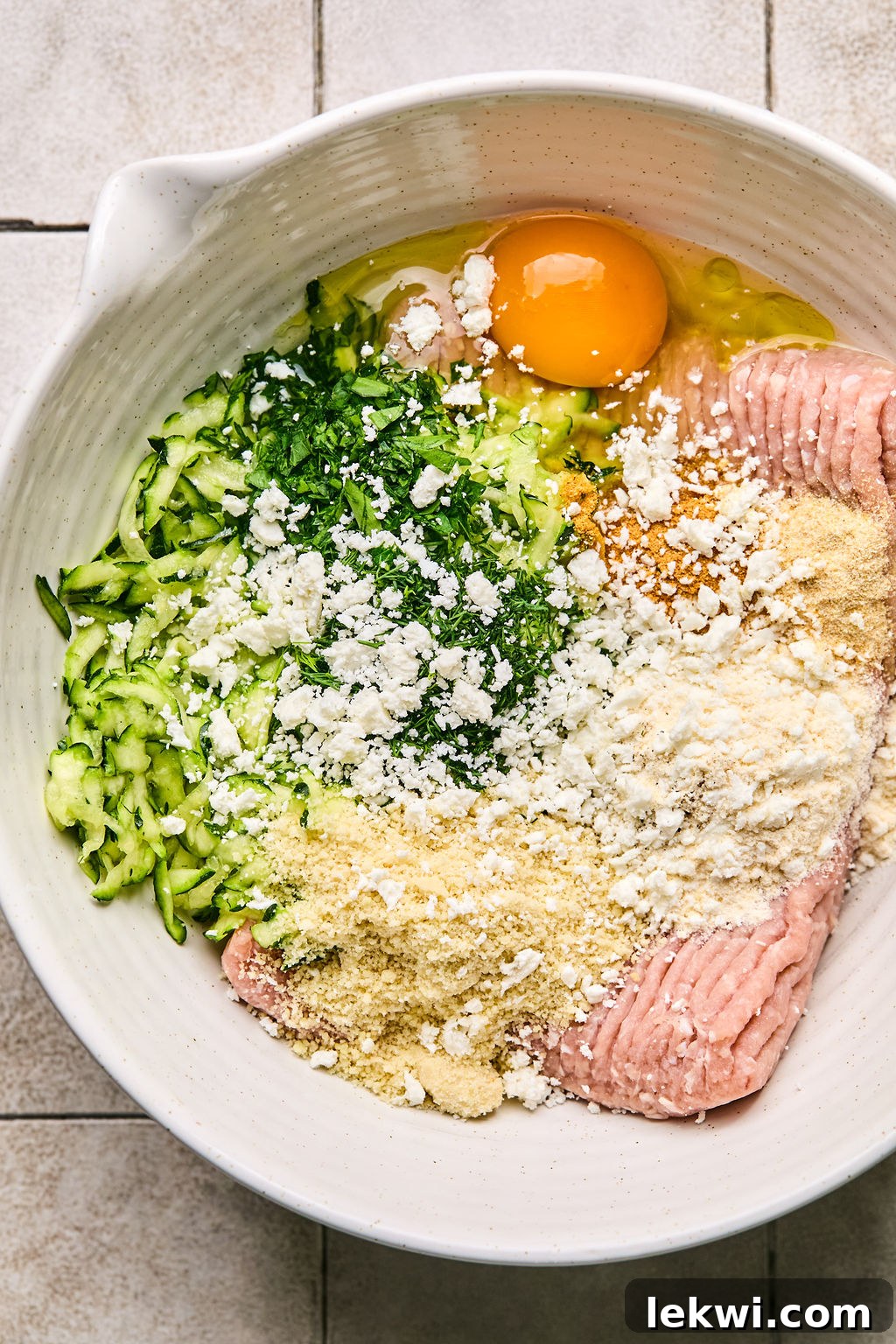 ground turkey, zucchini, almond flour, coconut flour, feta cheese, and herbs and seasonings in a bowl ready to be mixed