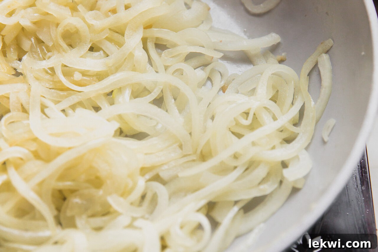 Thinly sliced yellow onions beginning to caramelize in a skillet with ghee, showing the initial stages of cooking.