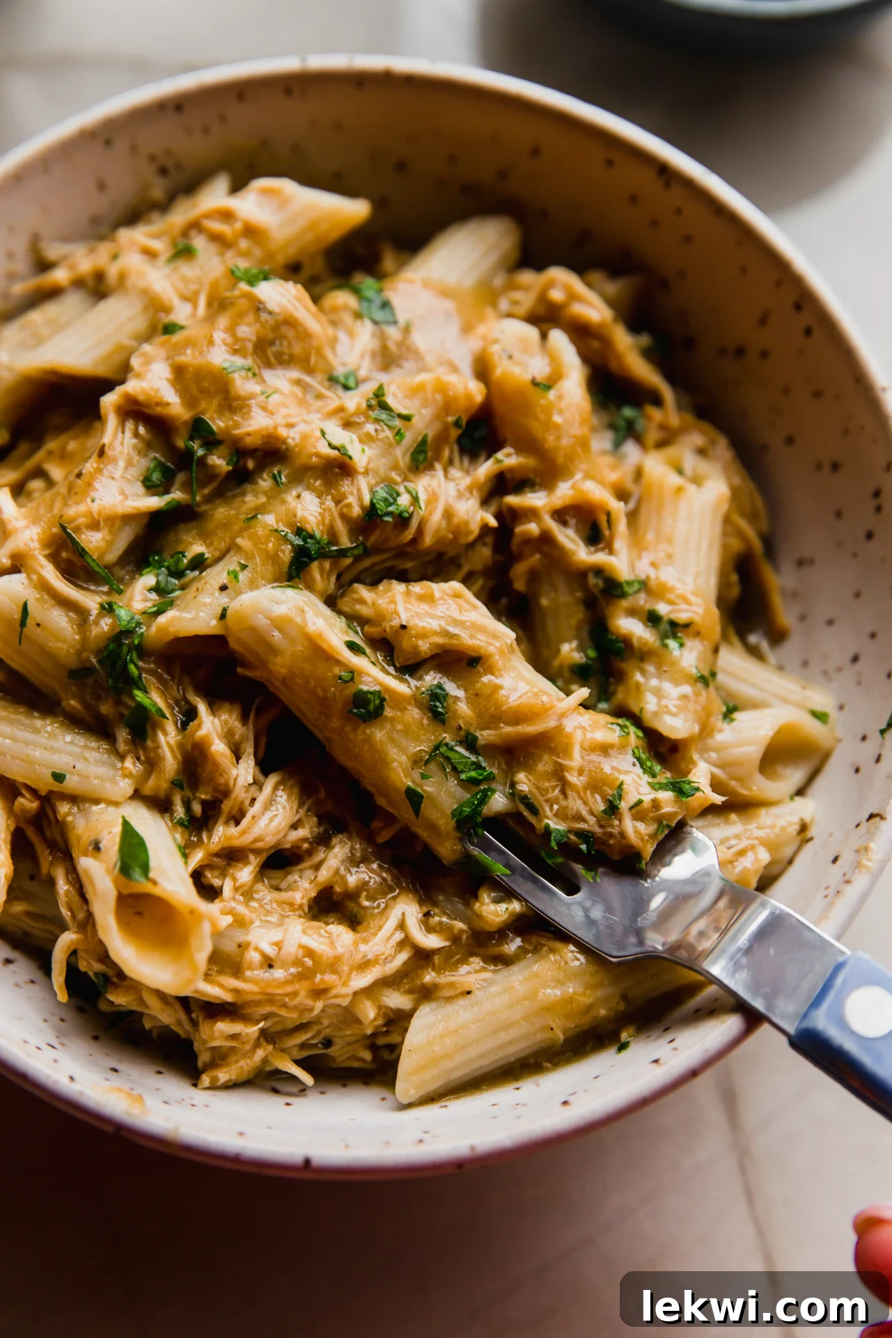 Slow cooker pasta served in a bowl with a fork and topped with fresh parsley, highlighting its creamy texture.