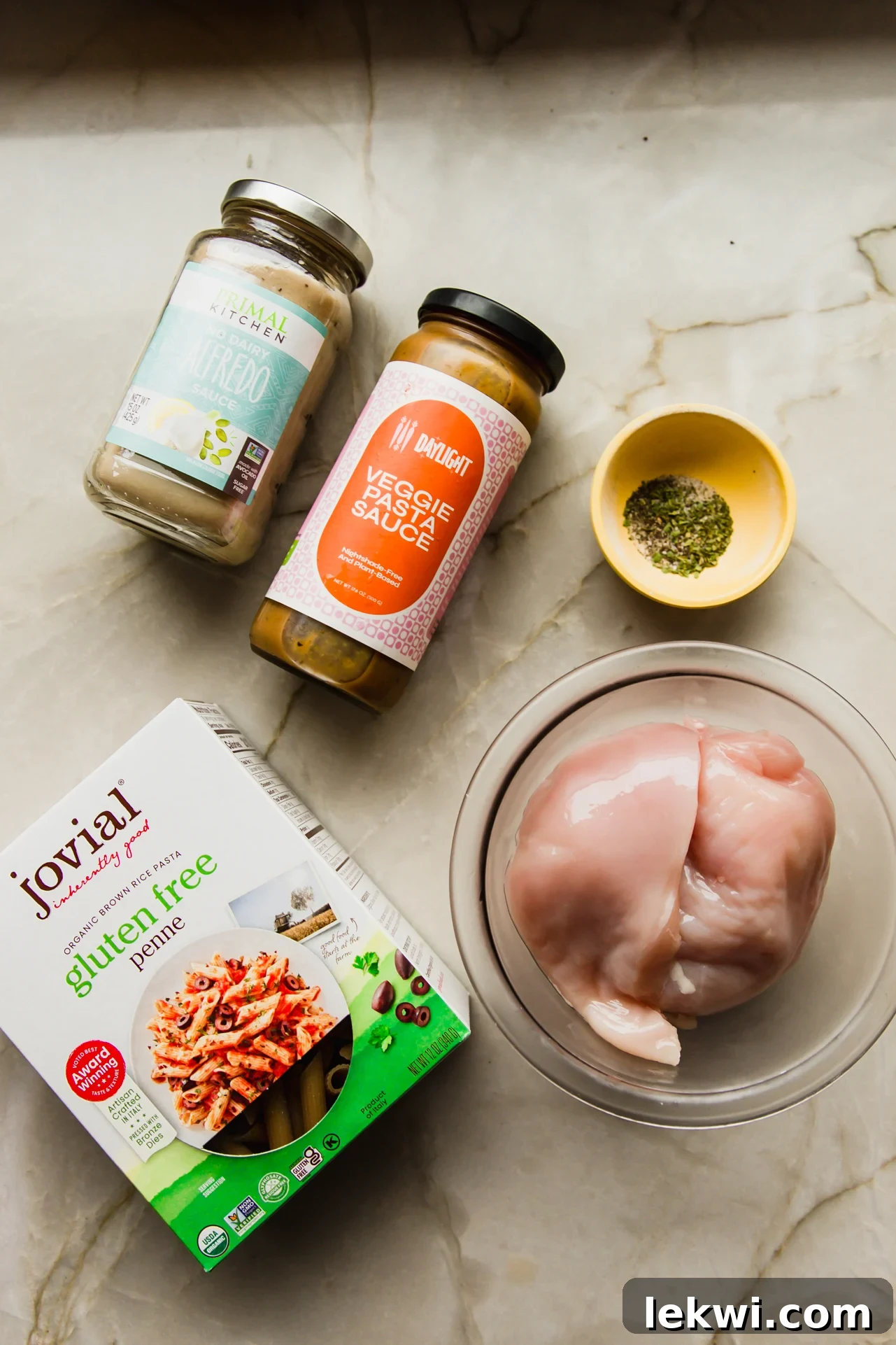 A selection of ingredients for creamy slow cooker pasta, including chicken, sauces, and pasta.