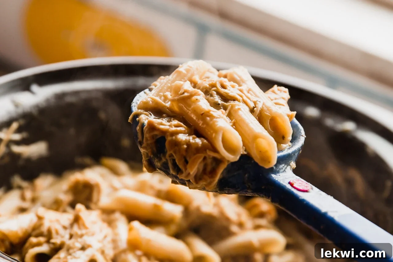 A spoon scooping creamy slow cooker chicken pasta, showing the well-coated noodles.