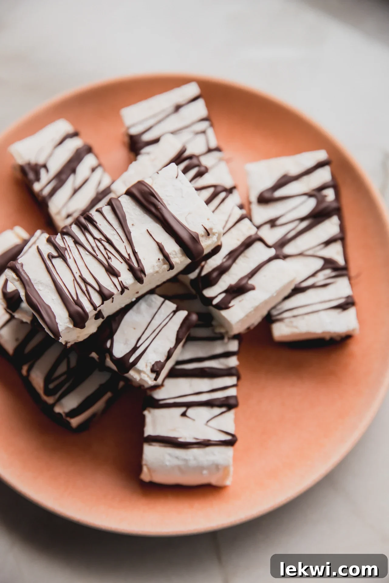 Marshmallow protein bars drizzled with chocolate and stacked on a pink plate.