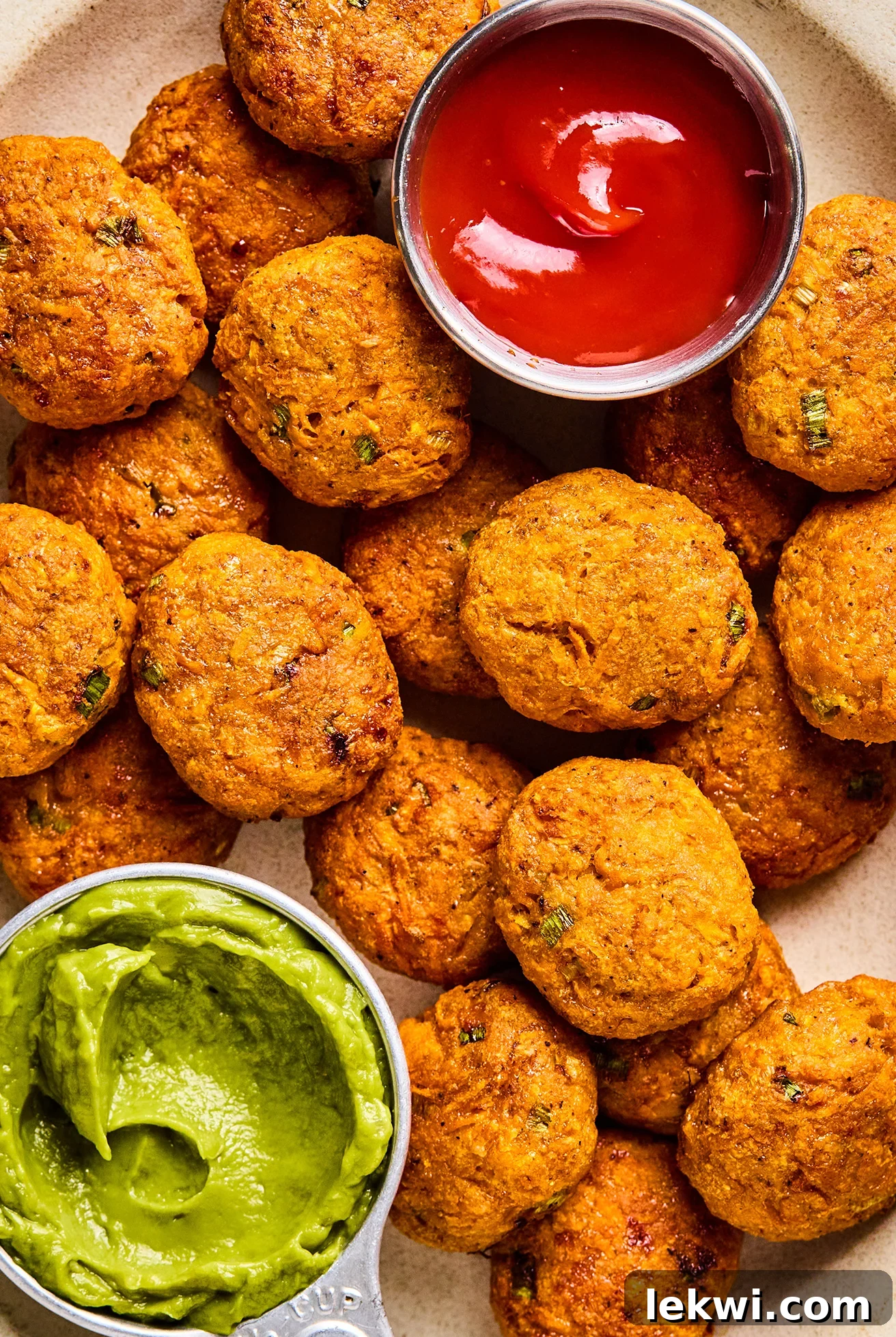 A plate of golden-brown Sweet Potato Chicken Poppers, served with a side of vibrant green guacamole and classic red ketchup, highlighting their delicious and dippable nature.