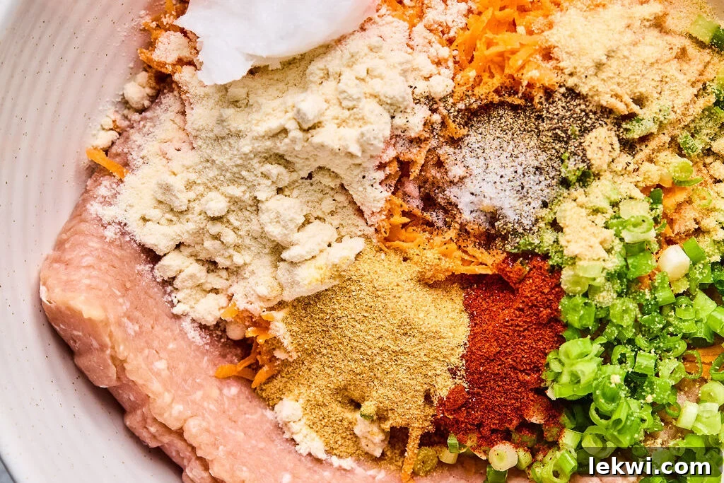 Ground chicken, shredded sweet potato, coconut flour, and spices are placed in a large mixing bowl, unmixed and ready for combining.