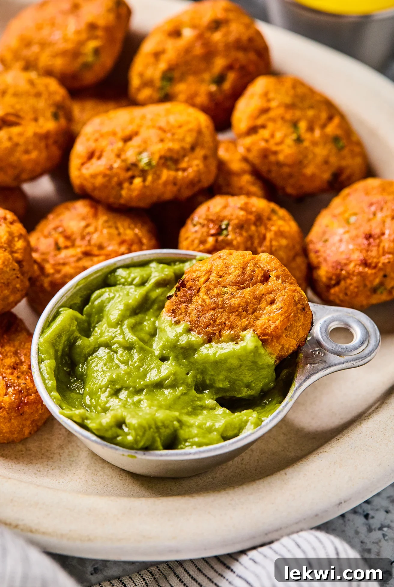 Sweet Potato Chicken Poppers on a white plate, with one popper being dipped into a small bowl of fresh guacamole, emphasizing their perfect size for dipping.