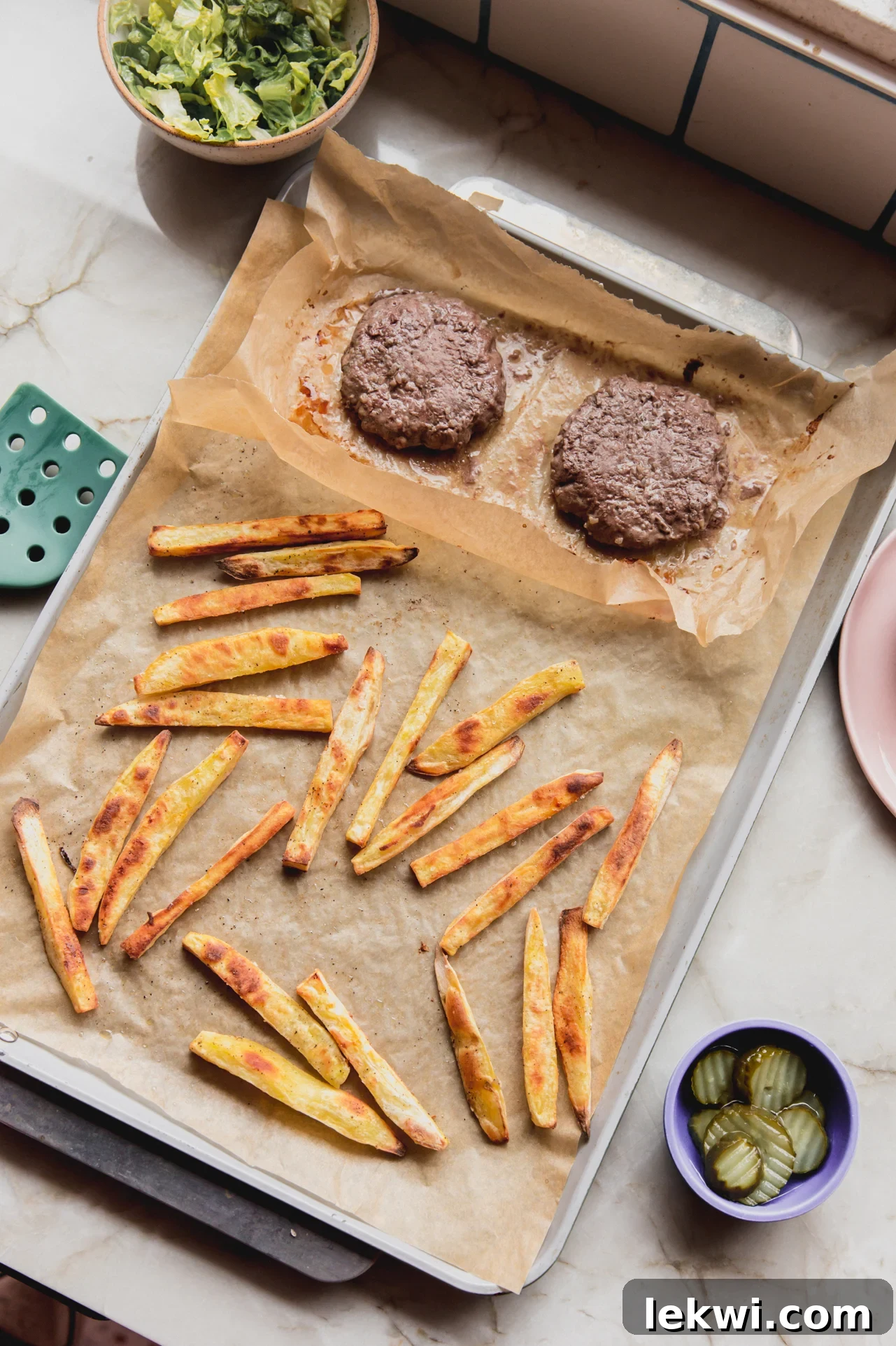 Freshly cooked sheet pan burger and fries, arranged neatly on parchment paper, ready to serve.