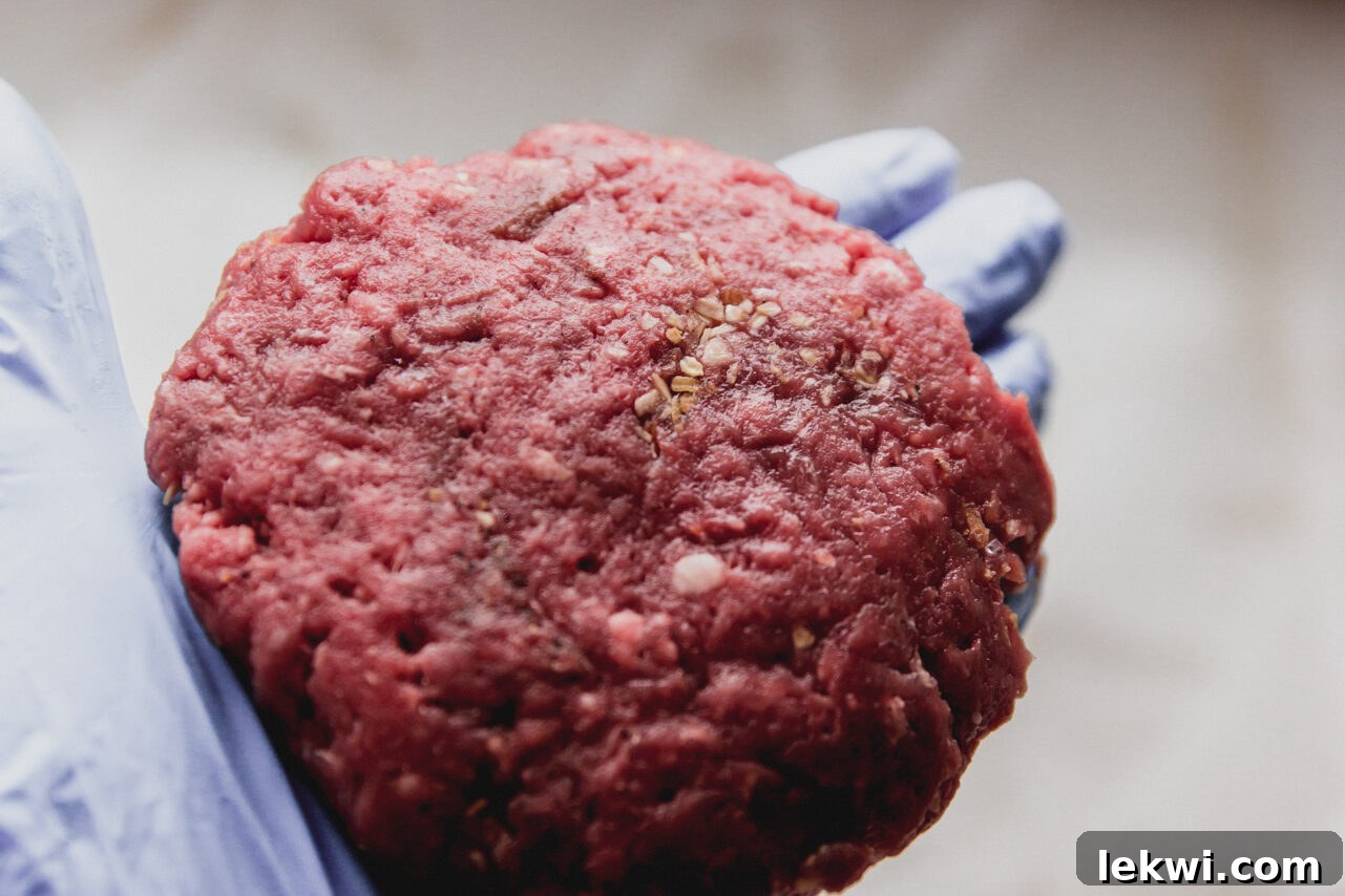 A perfectly formed raw burger patty held in a hand, ready for cooking.