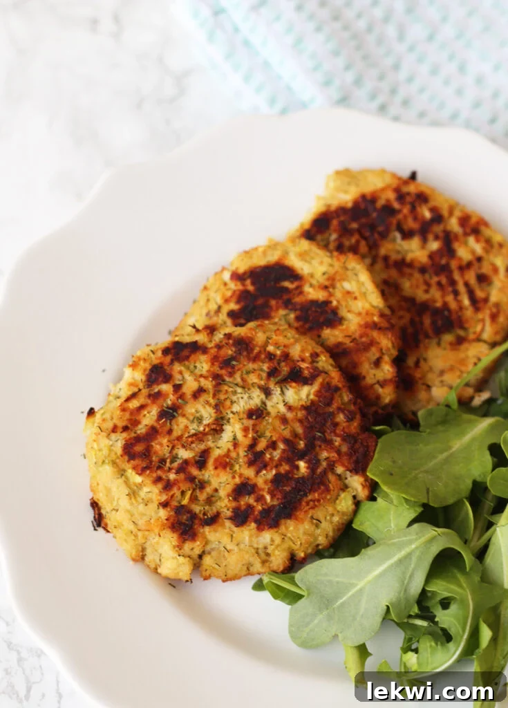 A plate with three salmon patties and arugula ready to be eaten.