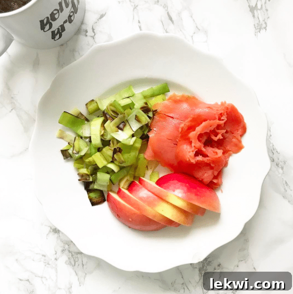 A breakfast plate featuring sliced apple, flaky smoked salmon, and a bed of fresh green arugula, beautifully arranged for a healthy meal.