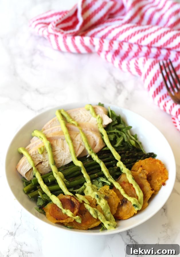 Nourishing Chicken, Asparagus, and Plantain Breakfast Bowl 3 A close-up view of the Chicken & Plantain Breakfast Balance Bowl, showing the textures of fried plantains, chicken, asparagus, and fresh greens, all generously topped with a vibrant dressing.