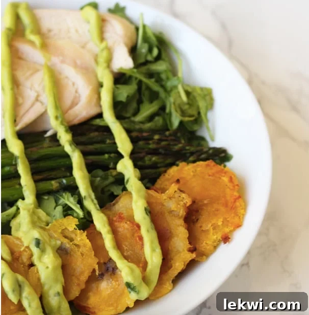 A bowl filled with fried plantains, chicken, aspargus, greens and topped with dressing.
