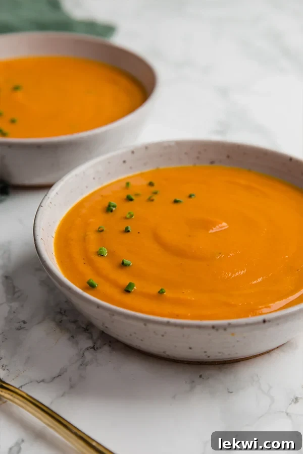 A ceramic bowl filled with carrot leek turmeric spring soup in it with another bowl filled with it behind it.