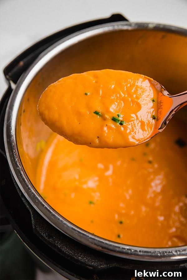 A spoon lifting a spoonful of carrot leek spring soup out of the pot with the soup in it.