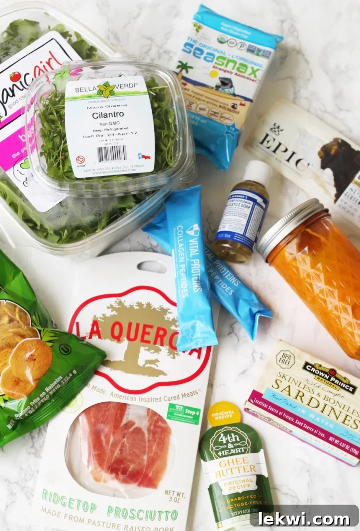 A curated selection of Paleo and AIP compliant travel foods, including fresh produce, snacks, and cooking essentials, laid out as part of a comprehensive guide.