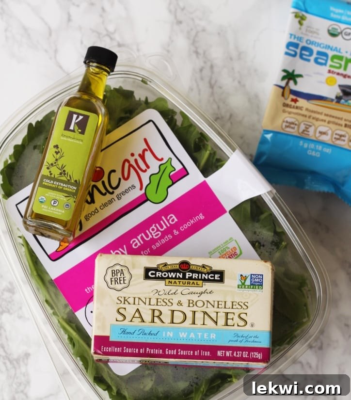 A container of crisp arugula, a bottle of olive oil, canned sardines, and a packet of seaweed snacks, ready to be combined for a quick and healthy meal.