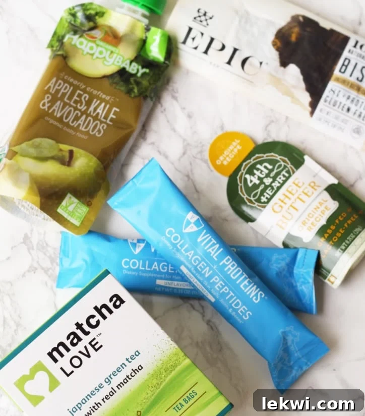 A collection of small, portable essentials for health-conscious travelers, including matcha tea, collagen packets, travel-sized ghee, and an Epic bar, arranged on a marble surface.
