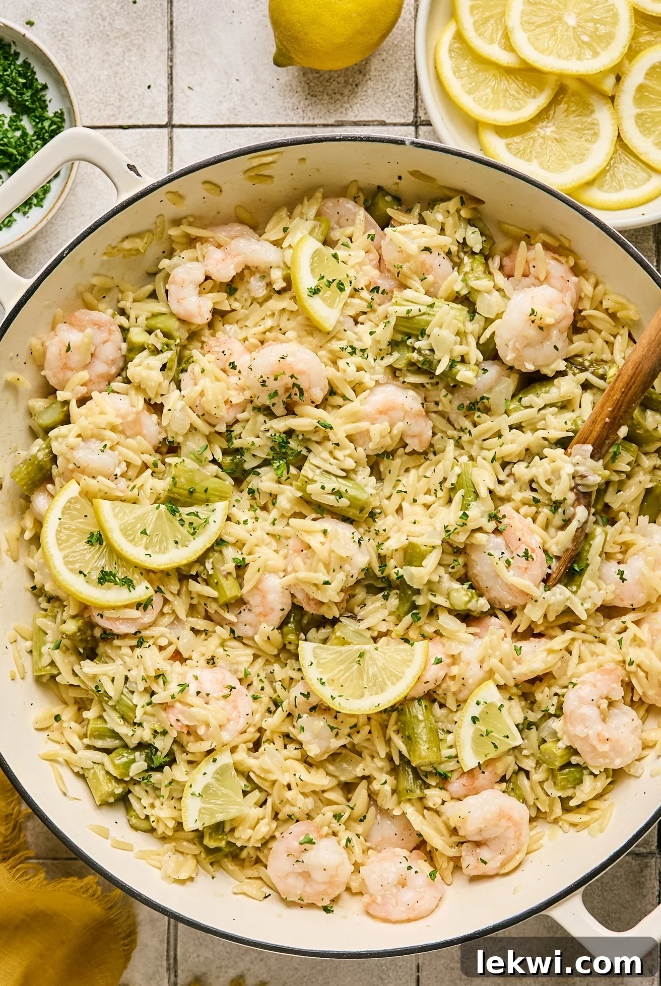 Gluten-free lemon shrimp and orzo served with sliced lemons in a large white cast iron pan, ready to be enjoyed.