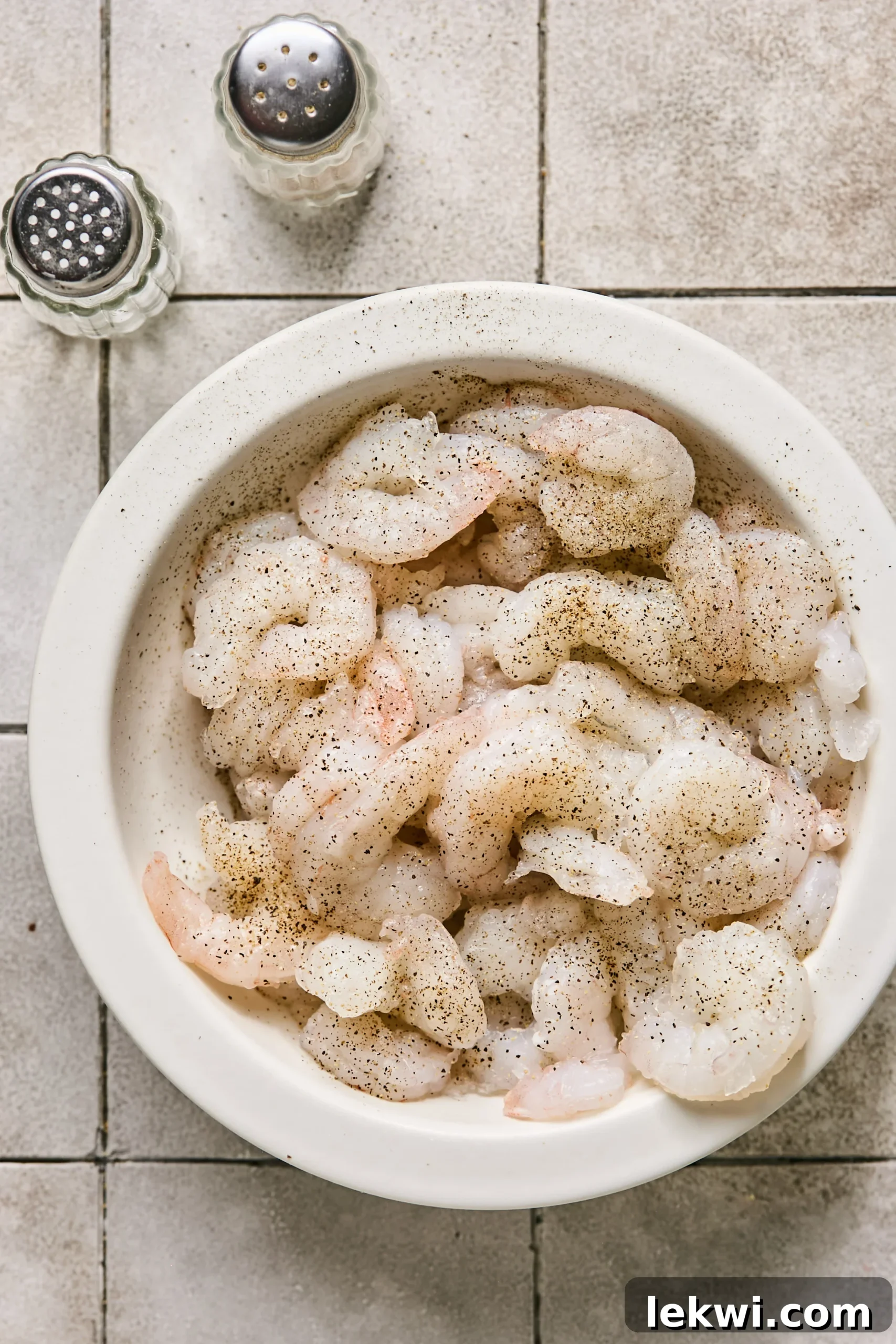 Raw shrimp meticulously seasoned with salt and pepper in a bowl, awaiting its turn in the hot pan.