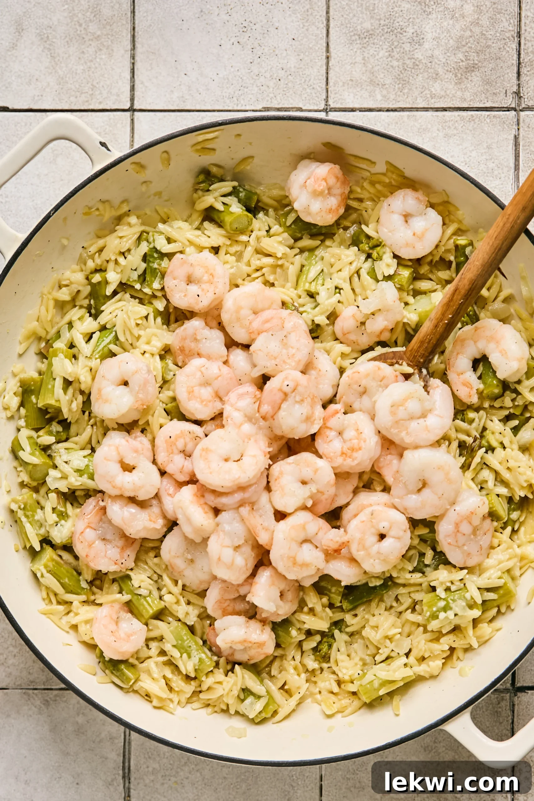 Shredded Pecorino cheese and cooked shrimp being gently folded into the creamy orzo and asparagus mixture in the pan.