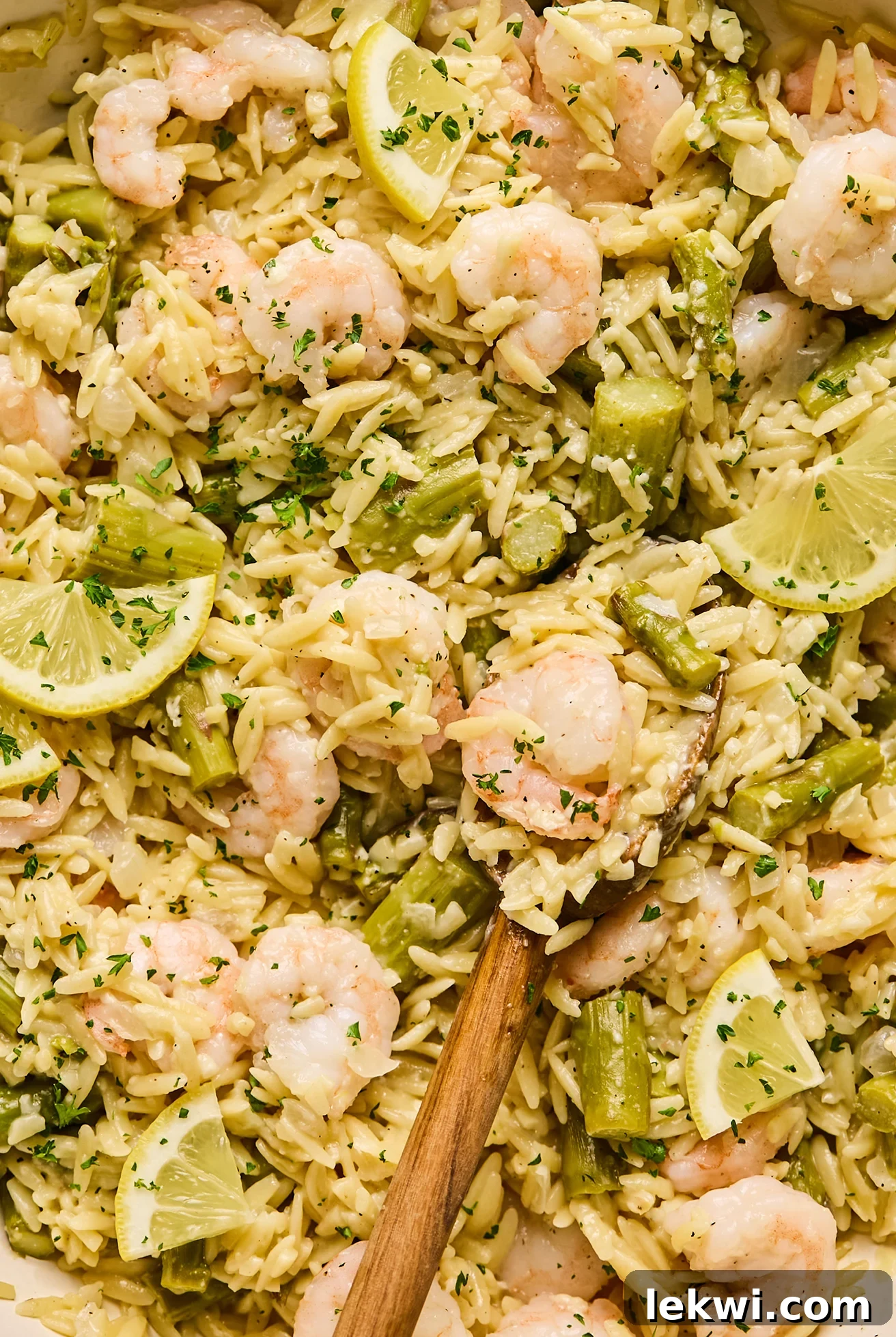 Gluten-free lemon shrimp and orzo beautifully plated and topped with fresh parsley and lemon slices, with a serving spoon tucked into the dish.