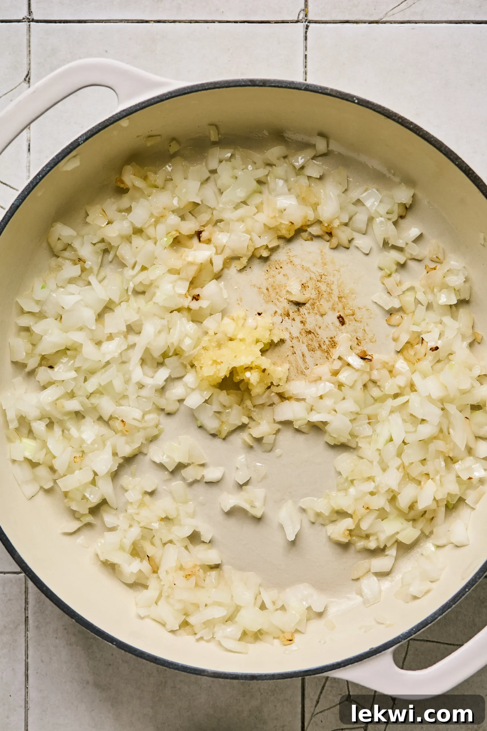Diced yellow onion and minced garlic being sautéed in a large deep pan until softened and fragrant.