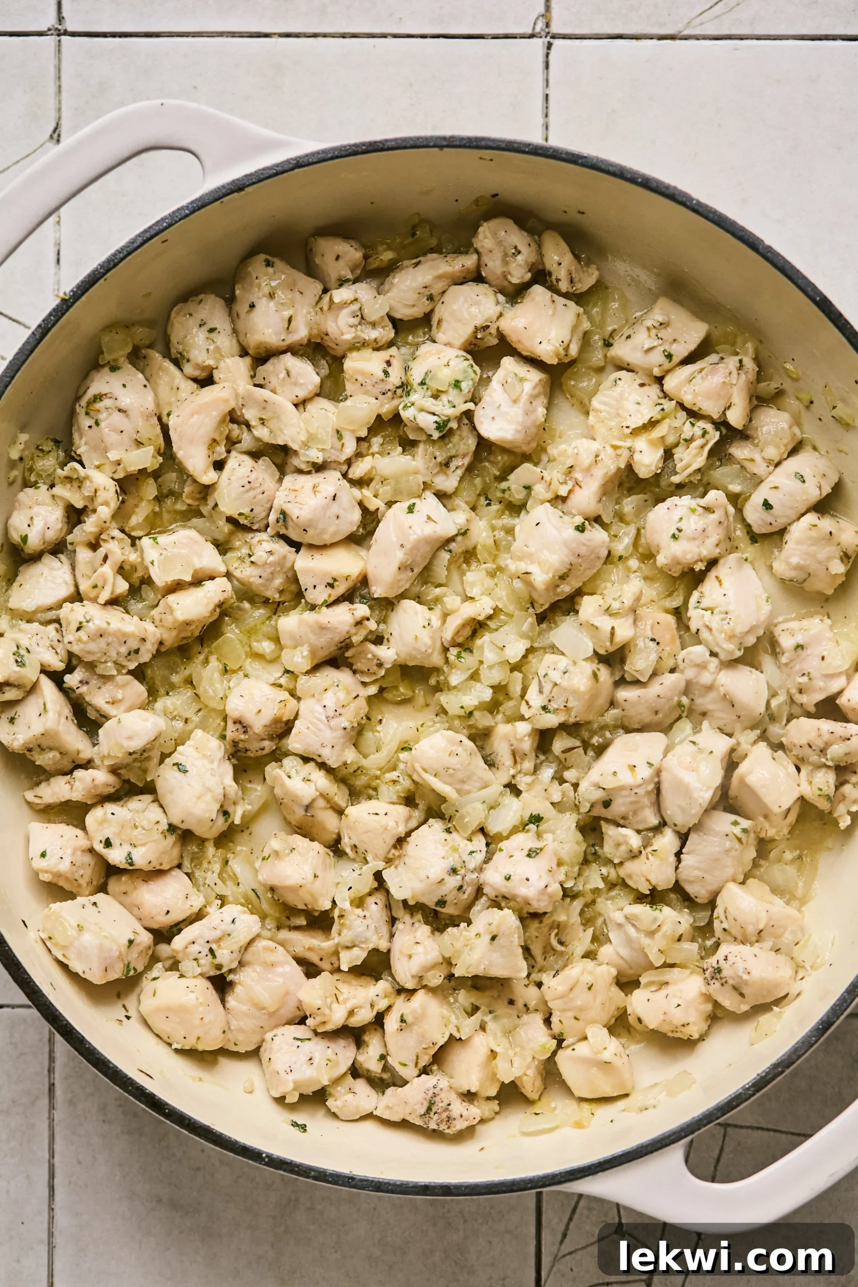 Cubed chicken breast added to the pan with sautéed onions and garlic, ready to be seasoned and lightly browned.