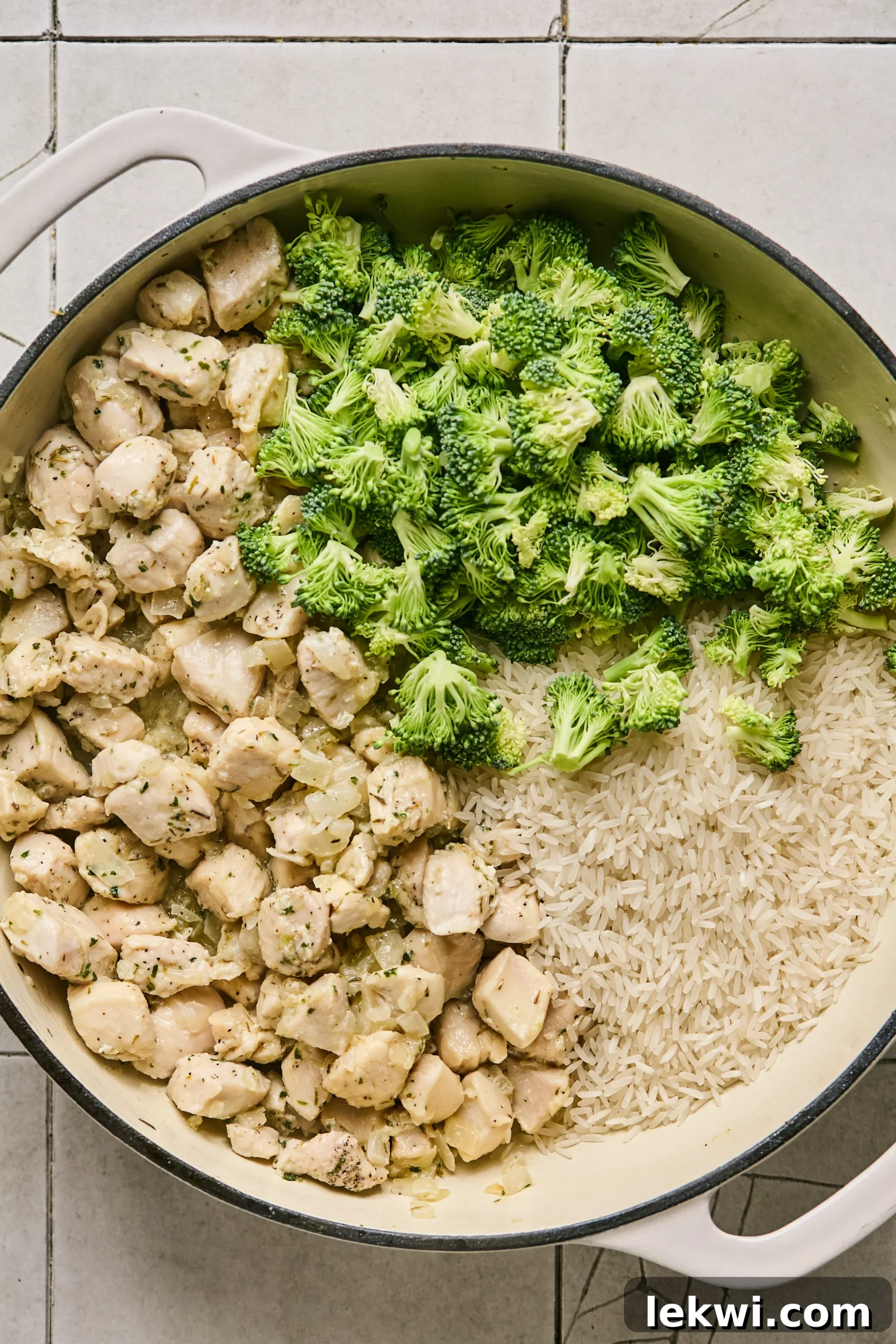 Rinsed jasmine rice and chopped broccoli florets being added to the pan alongside the partially cooked chicken, onions, and garlic.