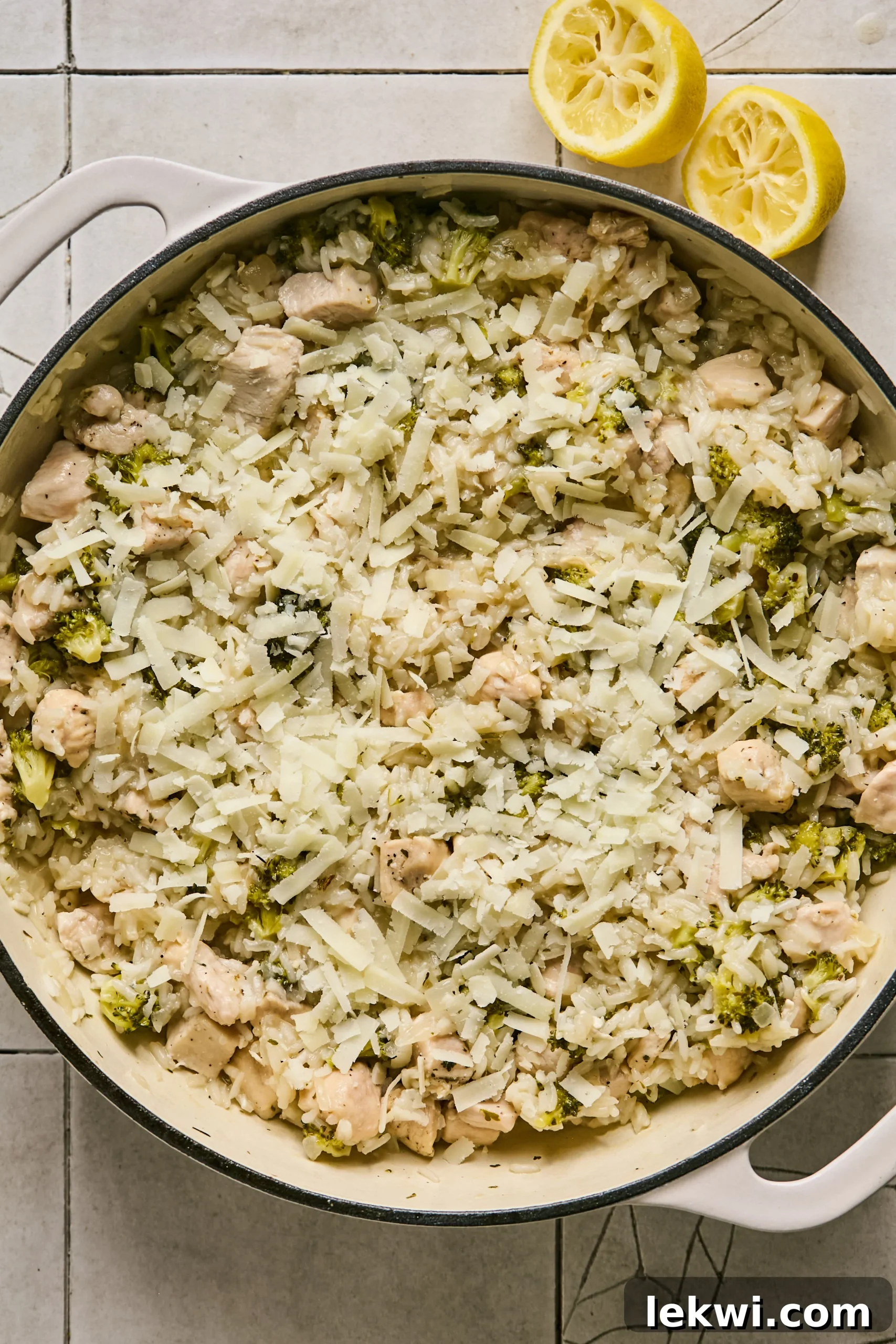 Shredded goat cheddar cheese being sprinkled over the cooked broccoli, chicken, and rice mixture in the pan.