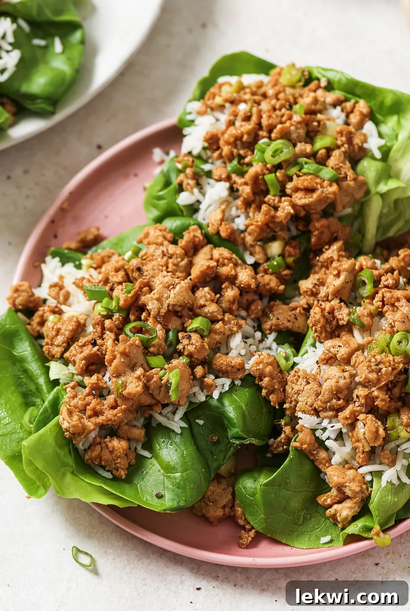 Ground orange chicken on a pink plate, served with rice in a lettuce cup.