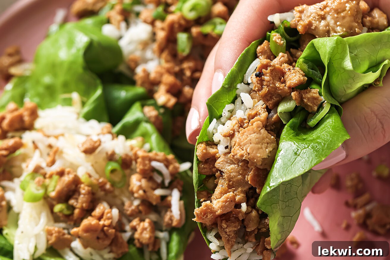 A hand holding an assembled orange ground chicken lettuce cup.