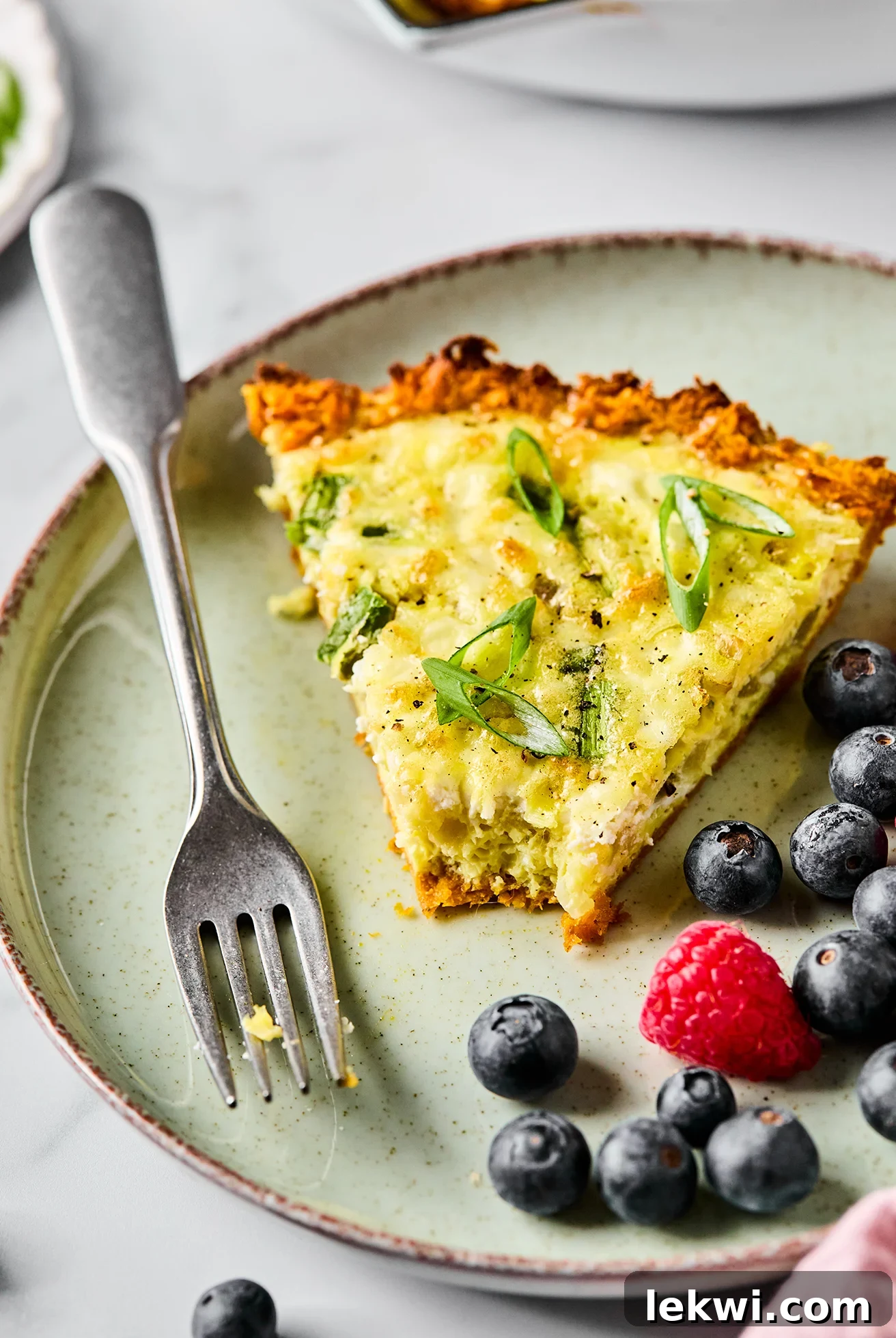 A close-up slice of sweet potato quiche, with a fork, showing the textured crust and savory filling.