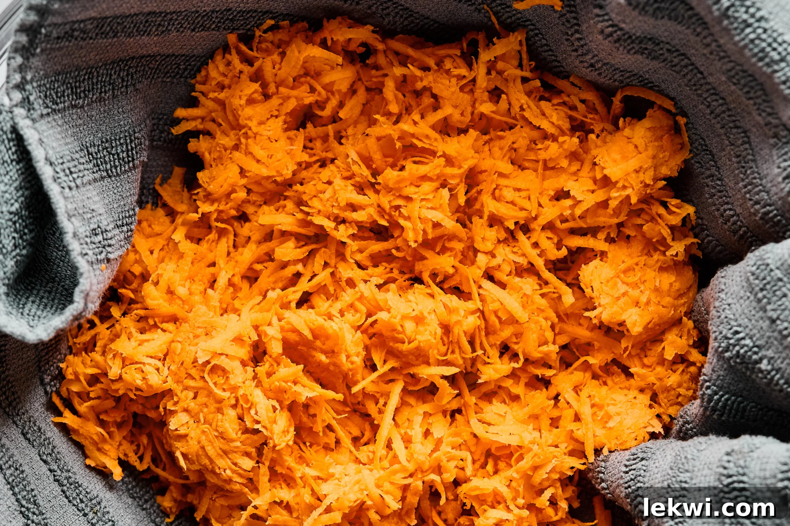 Shredded sweet potato in a towel, being squeezed to remove excess water.