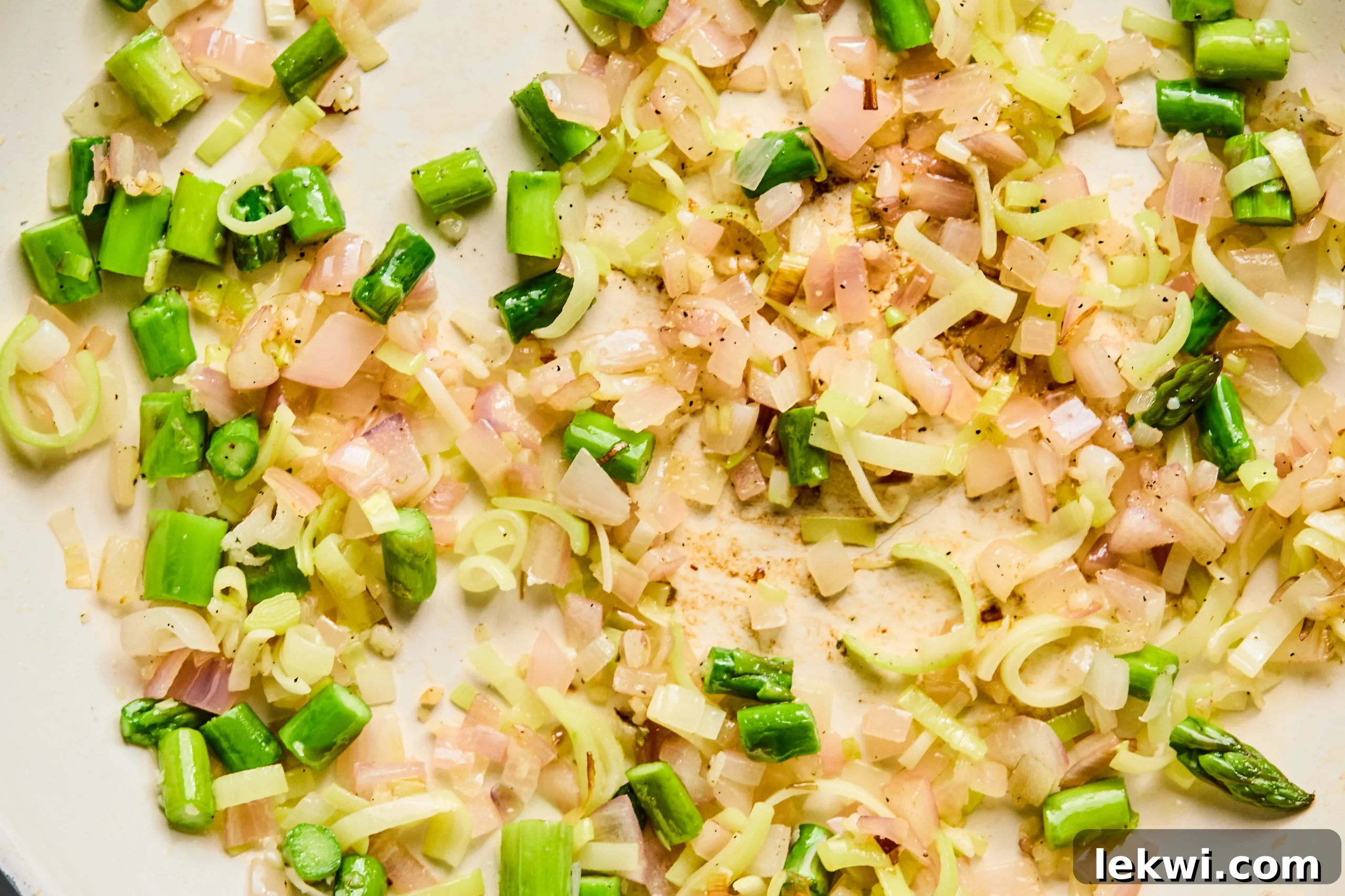 Chopped leeks, asparagus, shallots, and garlic sautéing in a pan.