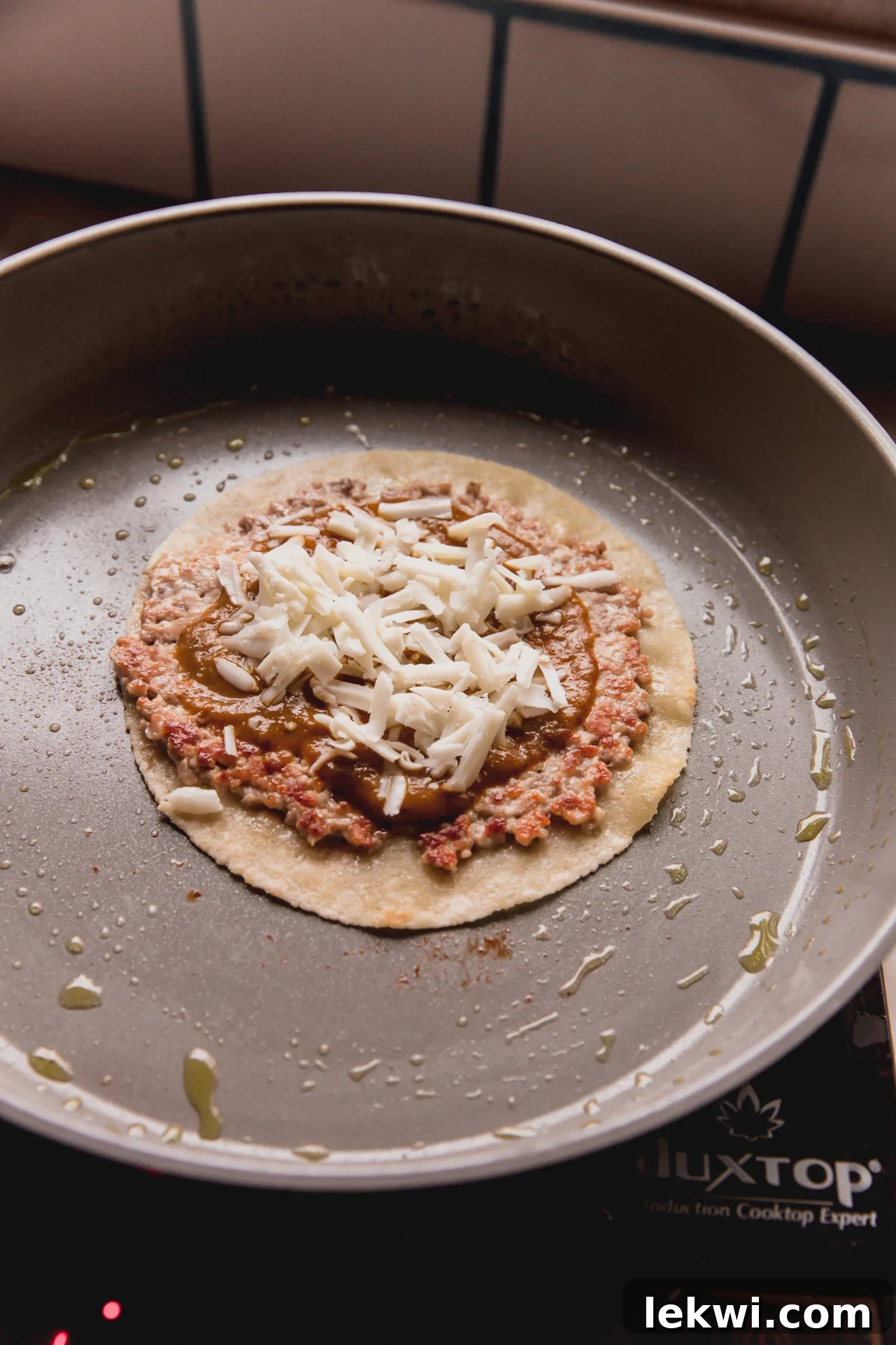 A cooked chicken parm smash burger taco in the pan, now topped with rich tomato sauce and shredded cheese, ready to melt.
