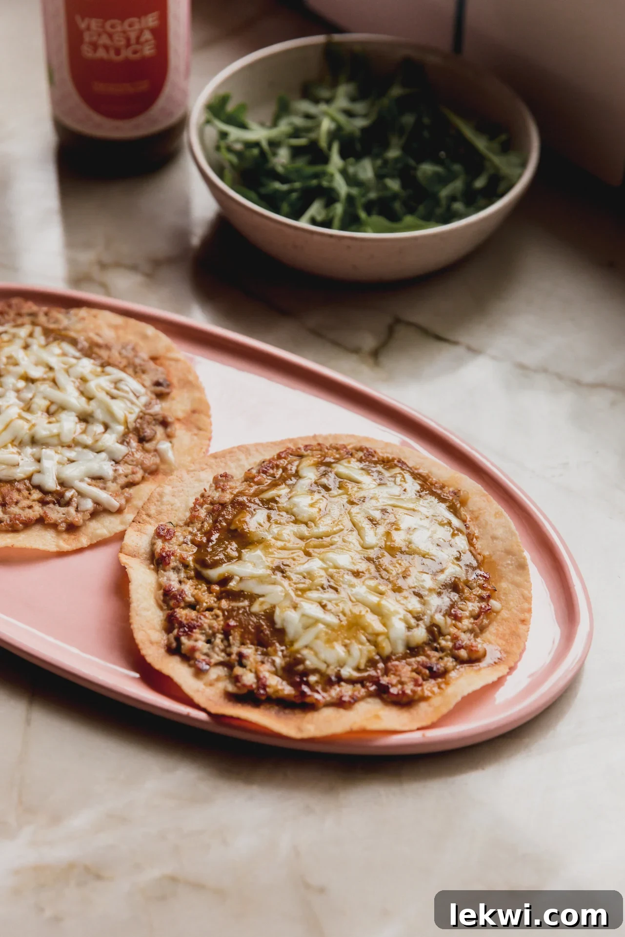 Two finished Chicken Parm Smash Burger Tacos on a serving dish, ready to be enjoyed, topped with fresh arugula.