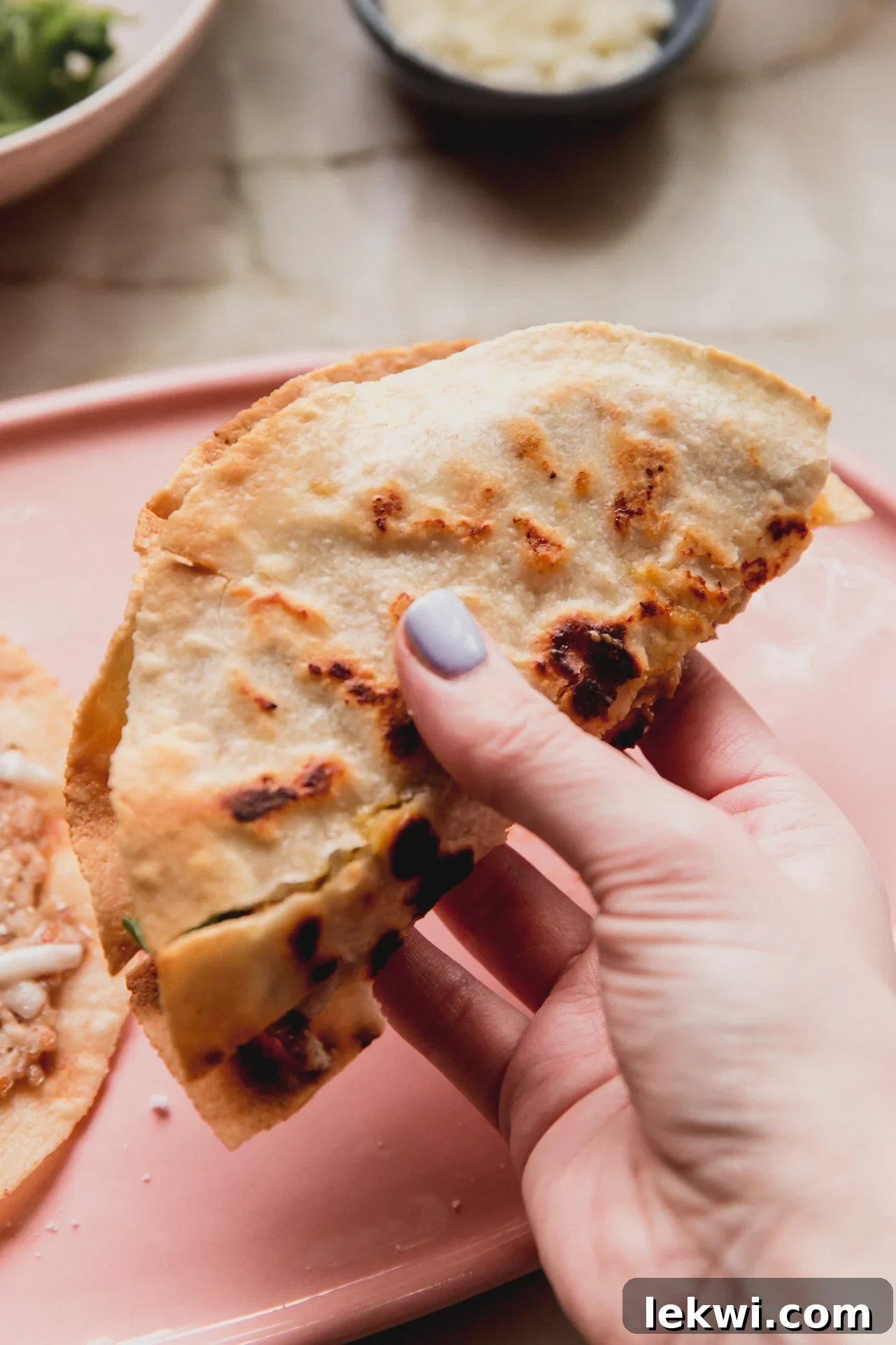 A hand holding a perfectly folded Chicken Parm Smash Burger Taco, ready to be eaten, showcasing its delicious layers.