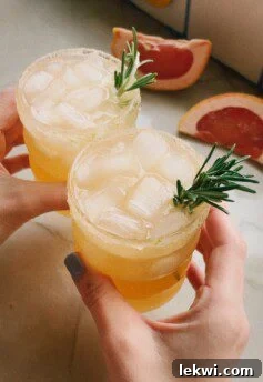 Two hands clinking glasses of grapefruit paloma mocktails in a celebratory toast.