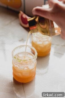 The vibrant mocktail mixture being poured from a cocktail shaker into a prepared glass filled with ice.