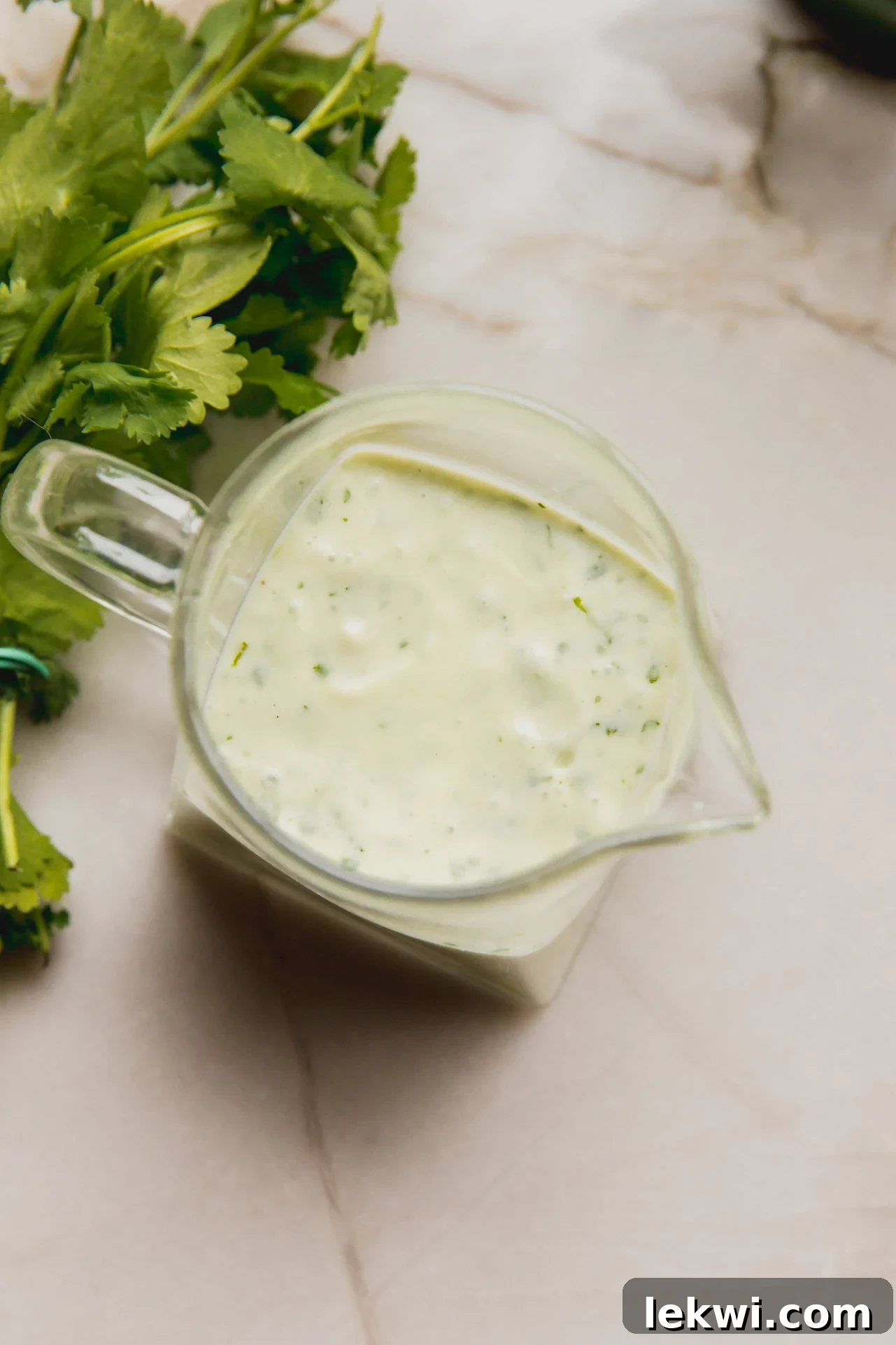 Taco salad dressing in a container with fresh cilantro sprigs in the background, ready to be served.