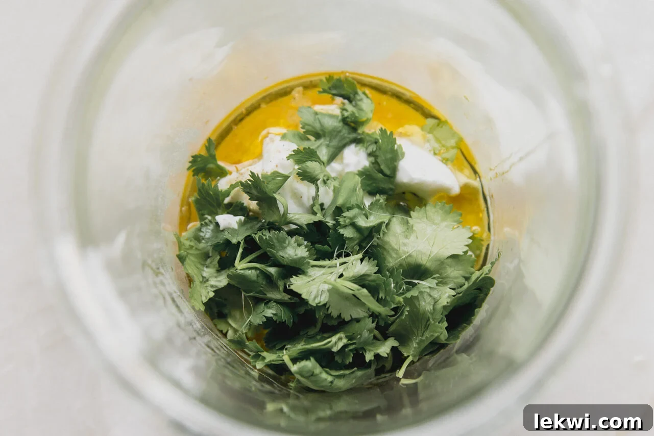 All the ingredients for homemade taco salad dressing, including coconut yogurt, lime, cilantro, and spices, gathered in a wide-mouthed glass jar before blending.
