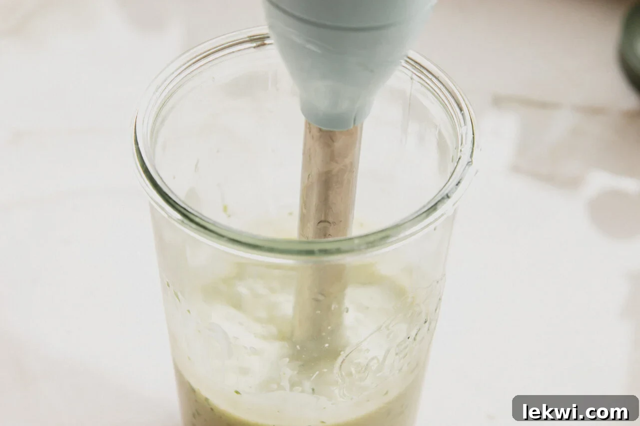 An immersion blender actively blending all the ingredients inside a glass jar, transforming them into a smooth, creamy homemade taco salad dressing.