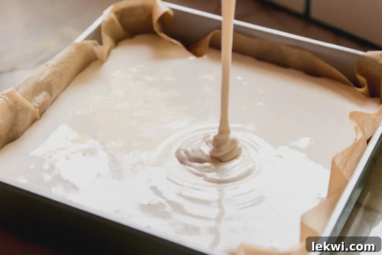 Pouring the prepared marshmallow layer into the baking pan over the cooled graham cracker crust.