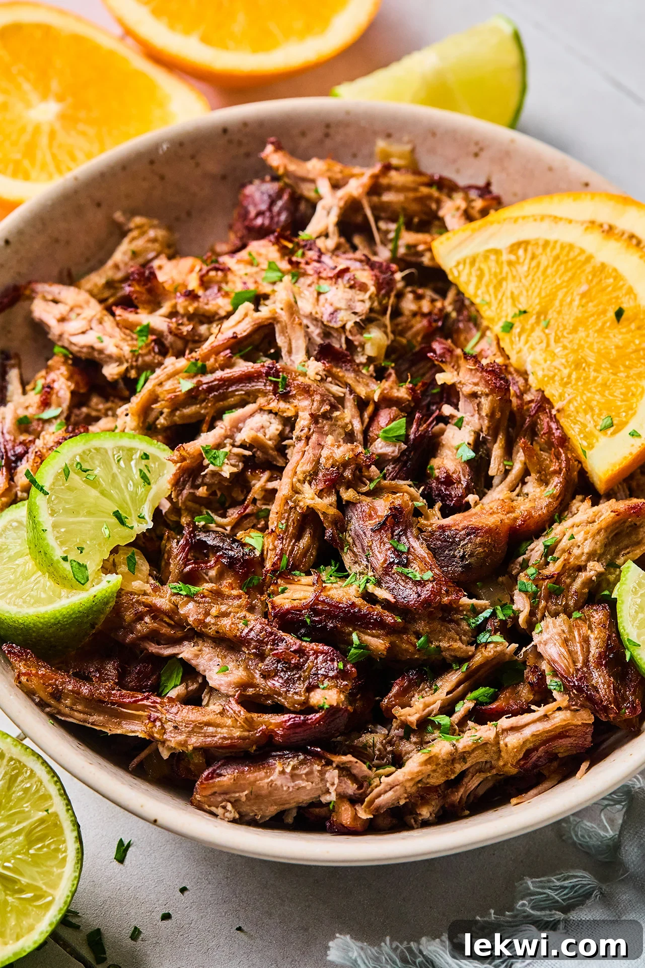 Slow cooker carnitas shredded in a bowl and topped with sliced lime, orange and chopped cilantro.