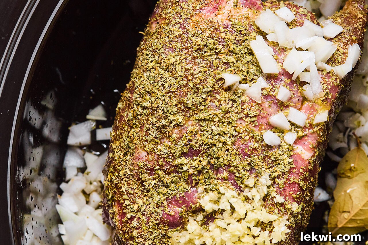 Pork shoulder in a slow cooker coated in a spice rub, with diced onion, minced garlic, and juice.